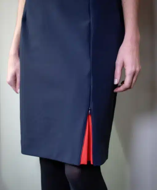 vue partielle d'une femme debout, portant une jupe marine s'ouvrant au bas de la jambe gauche sur une quille corail