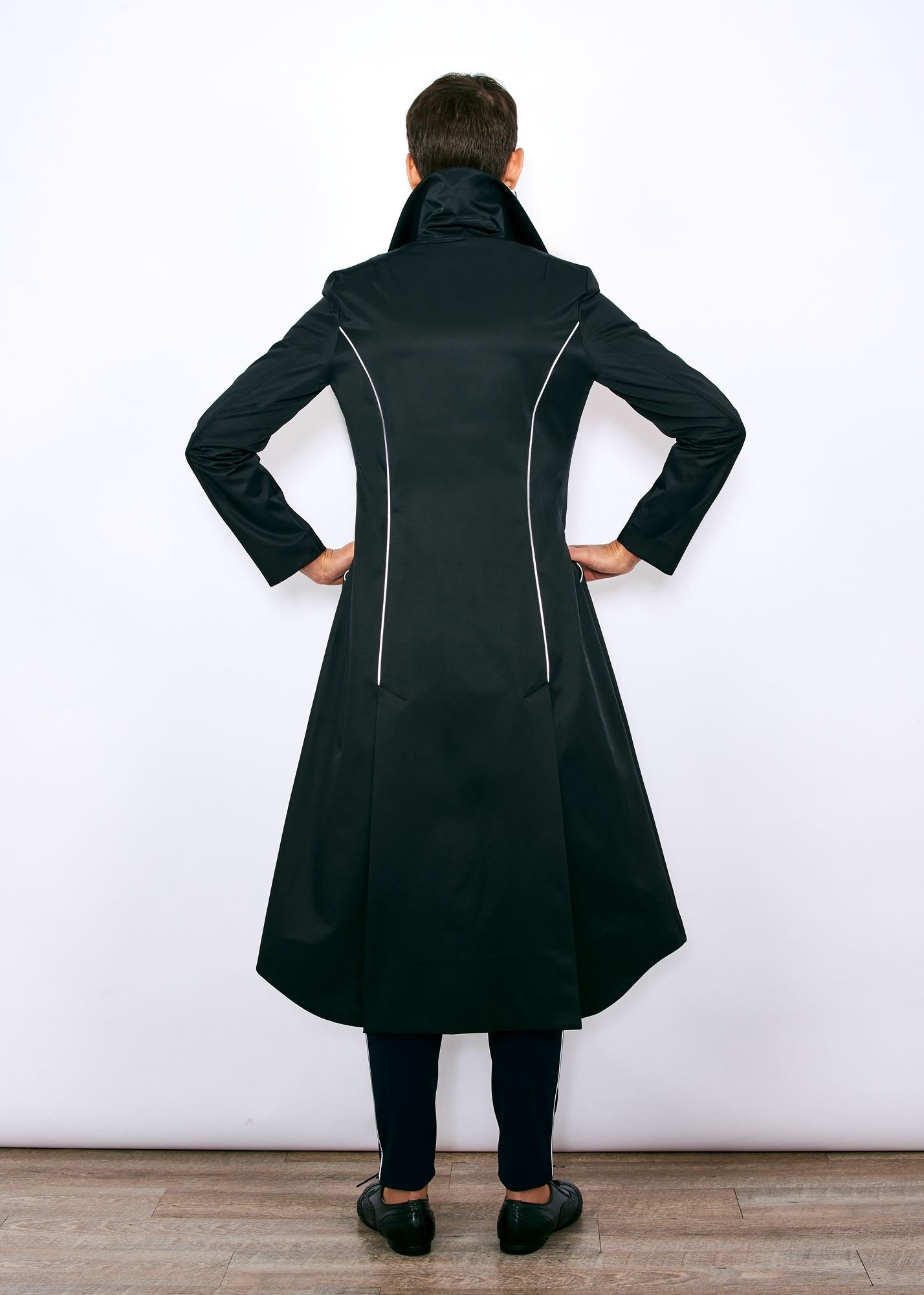 mannequin debout de dos, portant un trench long qui descent de dos jusqu'au mollets, col remonté, passepoils rétroréfléchiccants dans les 2 coutures dos, porté sur un pantalon marine