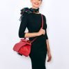 femme de 3/4 face portant une robe noire, col bateau couvrant les clavicules, manches 3/4, avec autour du cou un foulard fond noir et un sac rouge en bandoulière