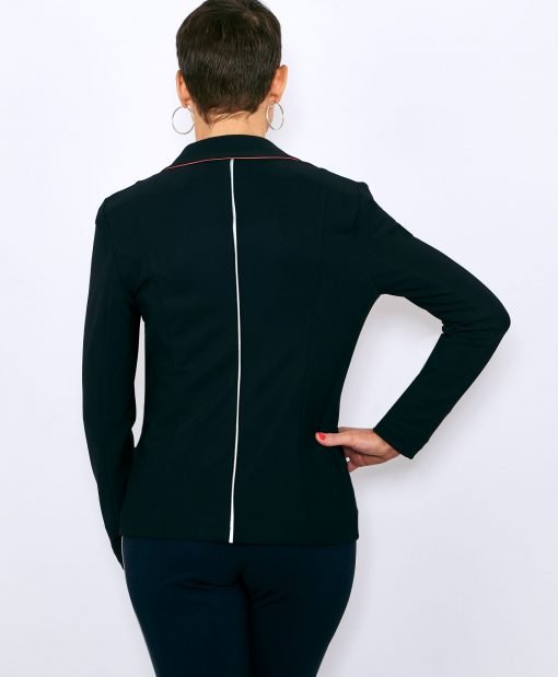 veste noire portée par une femme vue de dos, biais rétroréfléchissant vertical en couture, au milieu du dos, on aperçoit la couleur corail du dessous su col, main droite sur la hanche, pantalon marine