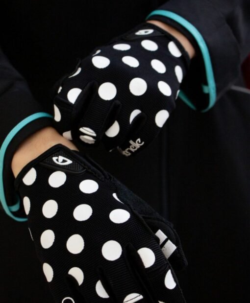 mains de femme portant des gants noirs à pois blancs, logo Giro au poignet et marque Cyclamelle sur le petit doigt
