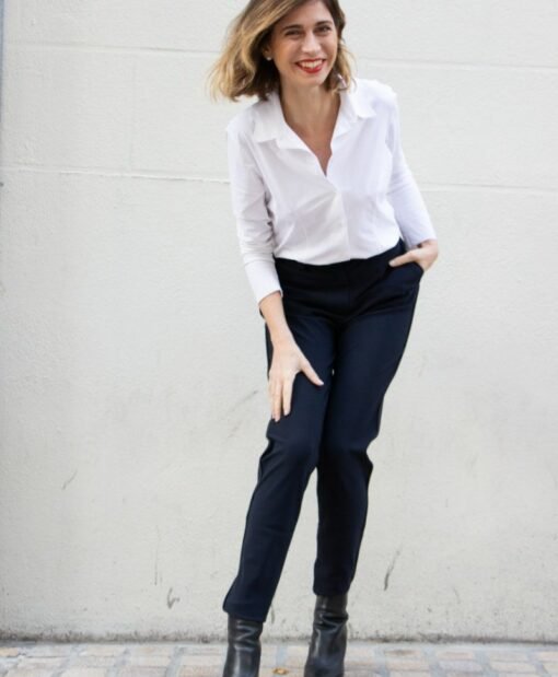 pantalon porté par une femme penchée vers l'avant, genoux pliés, chemisier blanc col ouvert porté manche 3/4 d'un côté, manche longue de l'autre