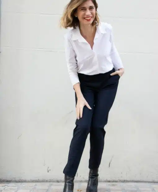 pantalon porté par une femme penchée vers l'avant, genoux pliés, chemisier blanc col ouvert porté manche 3/4 d'un côté, manche longue de l'autre