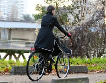 twin-jupe portée par une cycliste vue de dos, noire, bordée de bandes réfléchissantes pour la visibilité, partie longue devant, protégeant les jambes, partie courte derrière